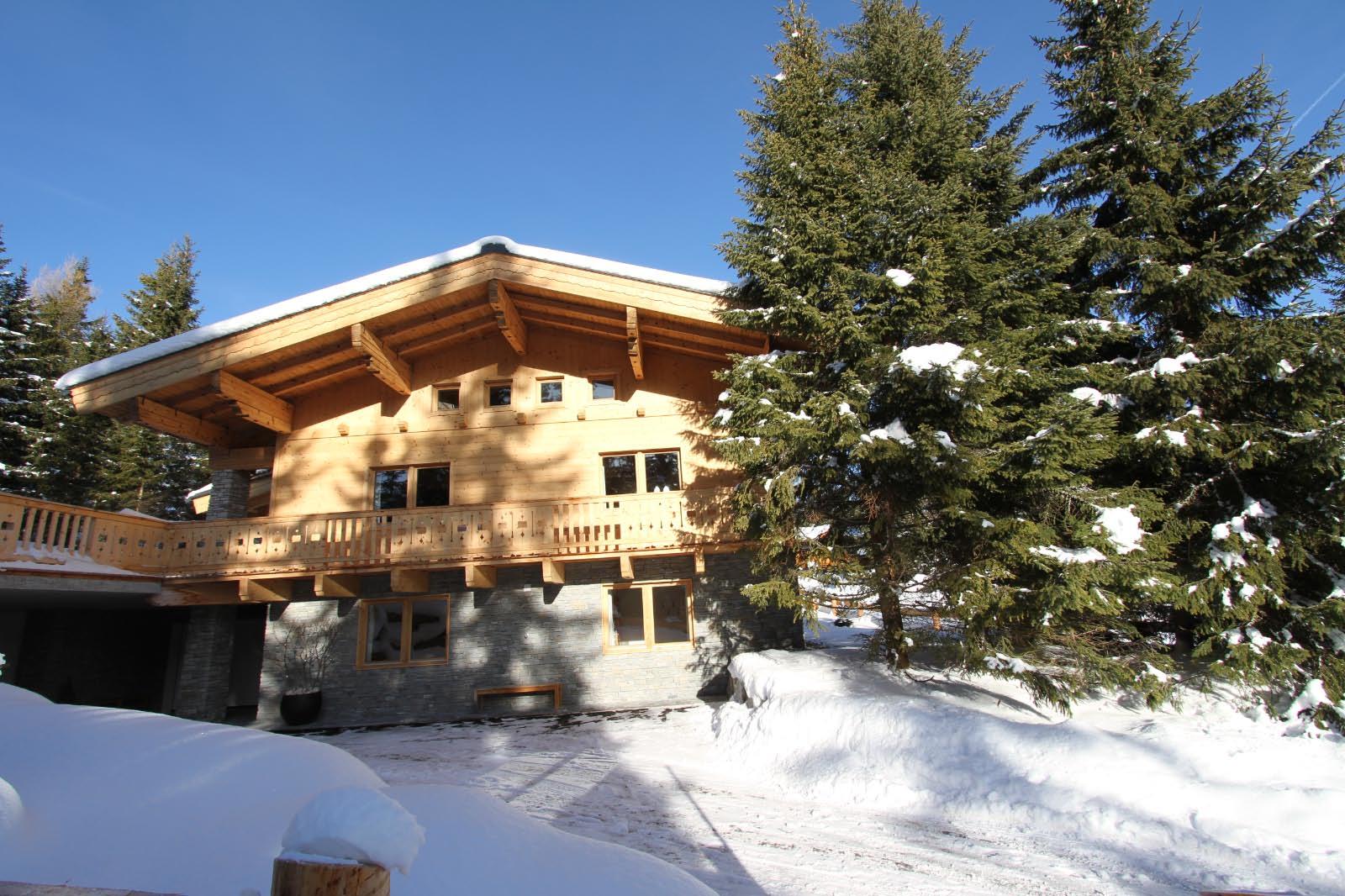 A cozy chalet surrounded by snow-covered trees. The sun shines on the wooden architecture of the house.