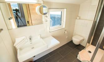 A modern bathroom with a shower, sink, and toilet. Bright tiles and a window create a friendly atmosphere.