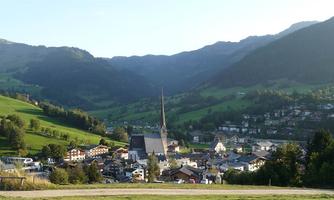 A picturesque village nestled in a green landscape with mountains in the background. The church with the tall tower is the central element of the image.
