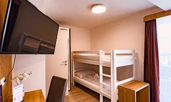 A simple room with a loft bed, a desk, and a television. The room has large windows with daylight.