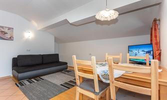 A cozy living room with a sofa, a dining table, and a television. The decor is modern and inviting, perfect for relaxing hours.