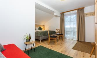 A cozy room with a double bed, a table, and chairs. Large windows provide plenty of natural light and a pleasant atmosphere.