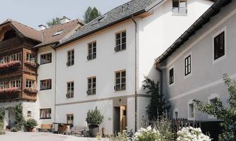A modern building with white walls and large windows.  
Plants and a cozy outdoor area give it an inviting character.