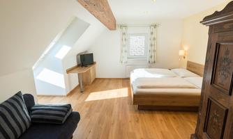 A bright and modern bedroom with wooden flooring and two beds. A sofa and a television are also in the room.