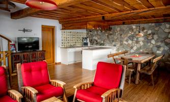 A cozy living space with red armchairs, wooden furniture, and a modern kitchen. The walls are adorned with natural stone, and the ambiance is warm and inviting.