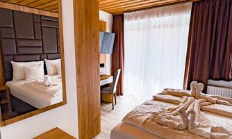 A modern hotel room with a wood ceiling and a large window. The bed is attractively decorated and there is a mirror and a desk.