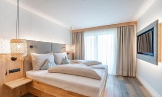 A modern bedroom with a large bed and soft colors. The window front lets in plenty of daylight and provides a cozy atmosphere.