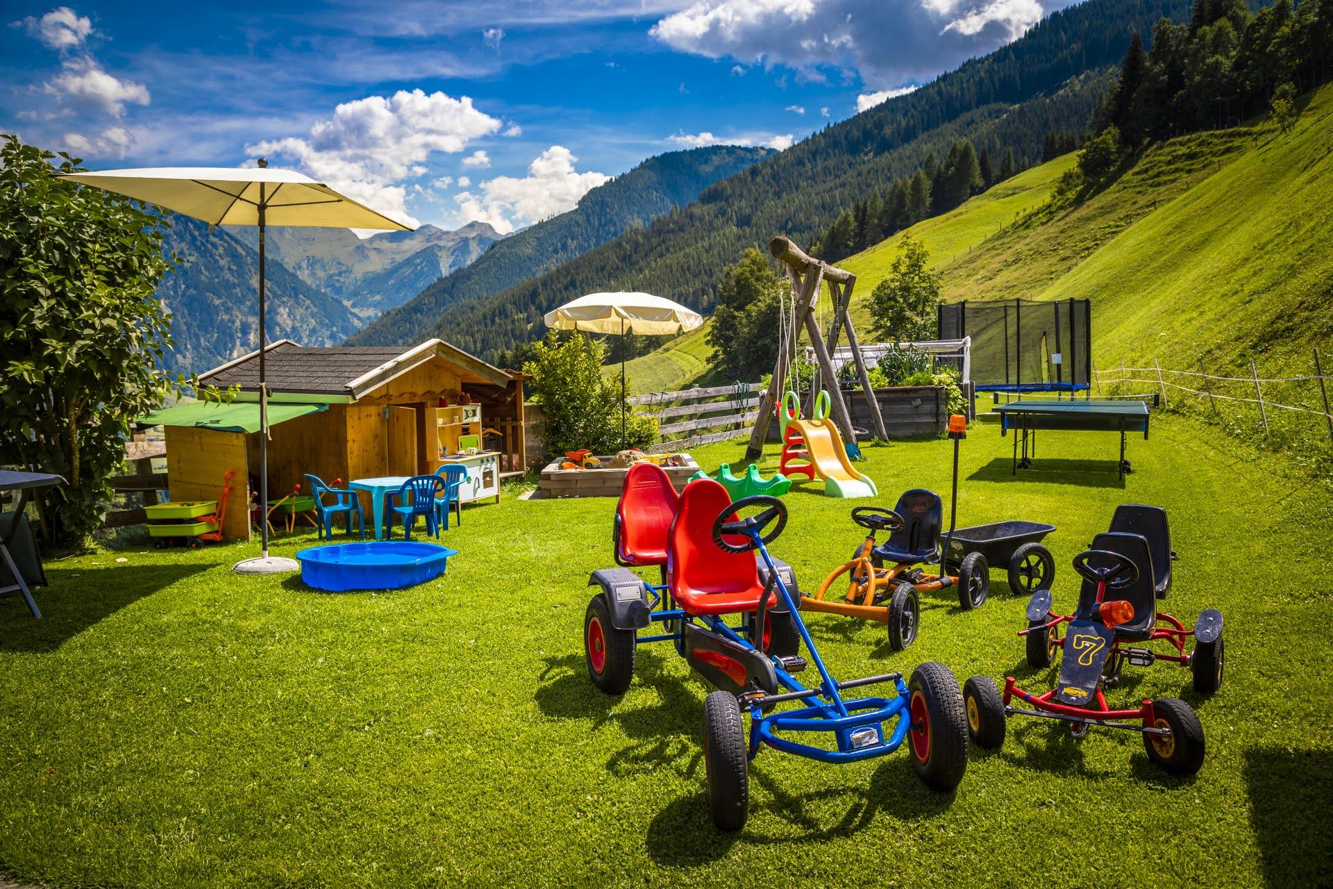 A playground with various go-karts on green grass. In the background, there are mountains and a beautiful sky visible.