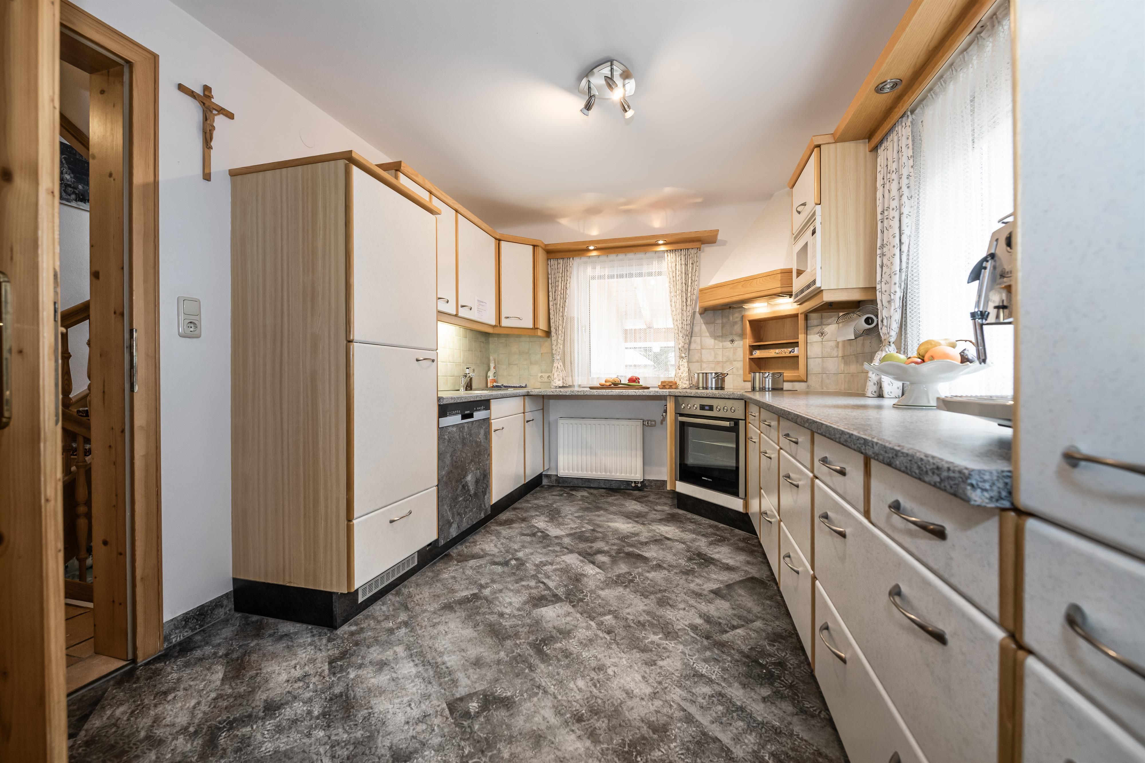 A modern kitchen with bright furniture and a large window front. The kitchen is well-equipped and features a refrigerator with freezer compartment, electric stove with oven, dishwasher, kettle, toaster, fully automatic coffee machine (whole beans are freshly ground), and plenty of dishes.
