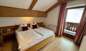 A cozy bedroom with two beds and wooden details. The window lets in a lot of light and offers a view outside.