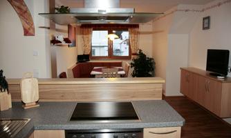 A modern kitchen with a cooktop and wooden shelves. In the background, there is a dining area with a table and chairs.