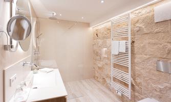 A modern bathroom with a shower, a sink, and bright stone walls. The atmosphere is bright and inviting.