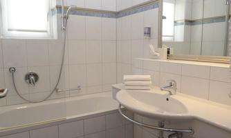 A modern bathroom with a bathtub and a sink. The walls are light tiled, and there is a large window for daylight.
