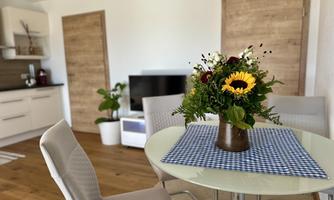 A cozy dining area with a round table and chairs. On the table, there is a beautiful bouquet of sunflowers.