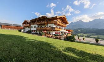 A cozy house in the Alps with several balconies and terraces. In the background, majestic mountains rise under a blue sky.