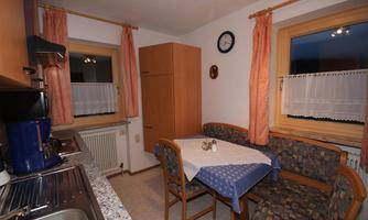 A cozy kitchen with wooden furniture and a round table. The windows are adorned with white curtains and let in plenty of light.