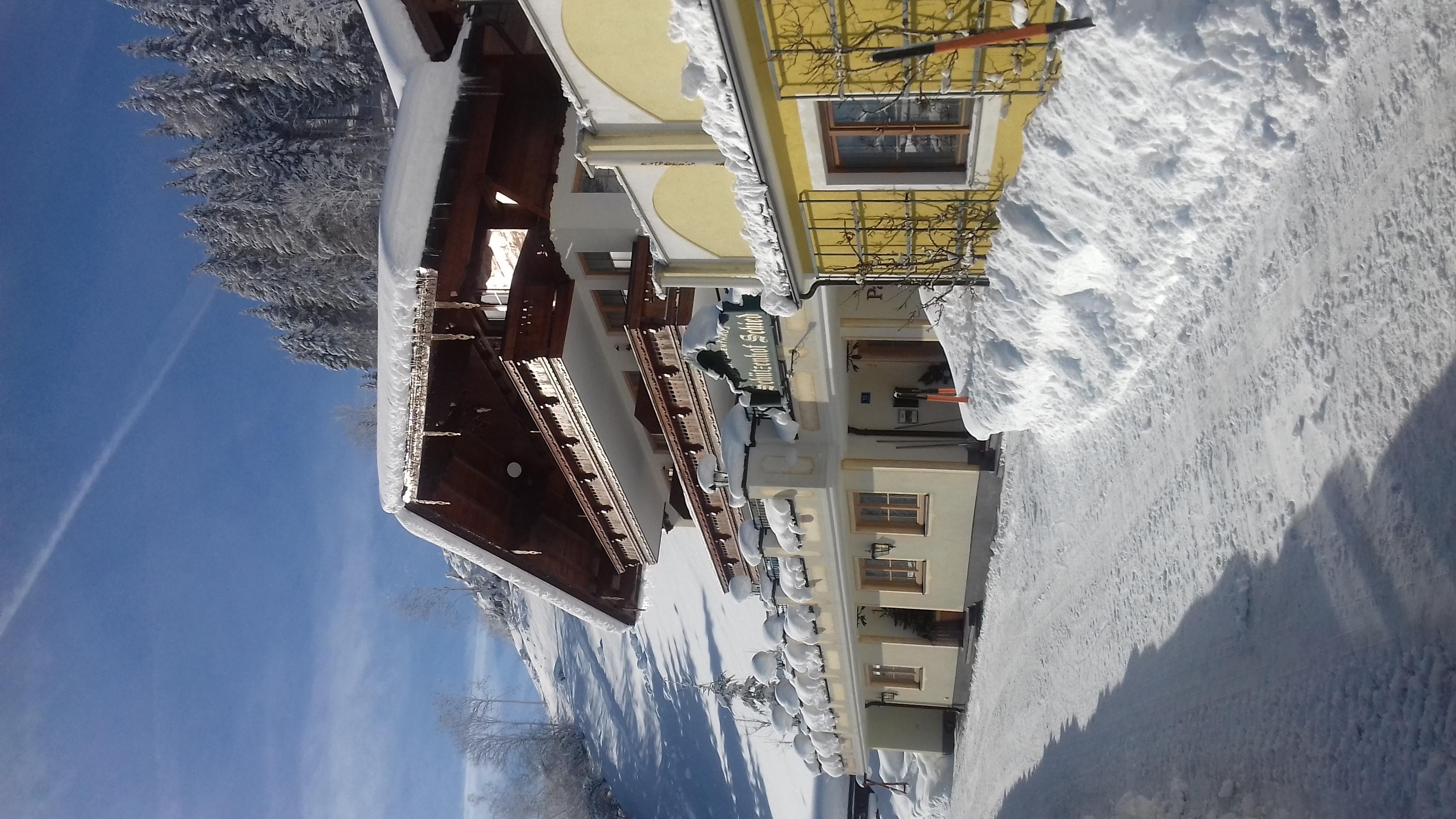 A charming, snow-covered chalet in the mountains. The sky is clear and blue, surrounded by snowy trees.