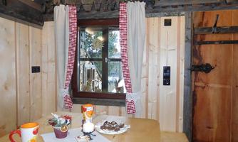 A cozy cabin with wooden cladding and a window adorned with checkered curtains. Drinks and sweets are on the table.