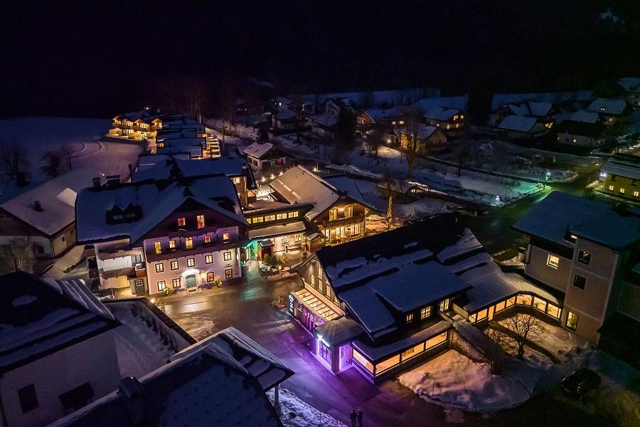 A picturesque winter landscape with illuminated buildings in a snowy town. The night sky creates a cozy atmosphere.