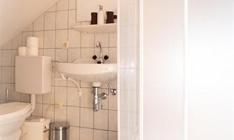 A small bathroom with a shower, toilet, and sink. The walls are brightly tiled, and there are some bathroom accessories on a shelf.