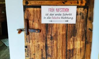 An old wooden door with an inscription. The message humorously alludes to getting up early.