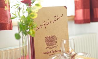 A table with a menu from the Edelweiss inn, decorated with a rose and flowers. The room is designed to be friendly and inviting.