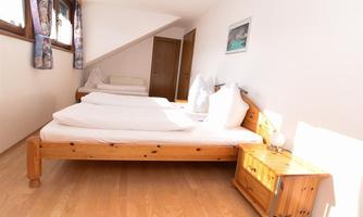 A bright room with wooden furniture and a double bed. Next to the bed is a nightstand with a lamp.