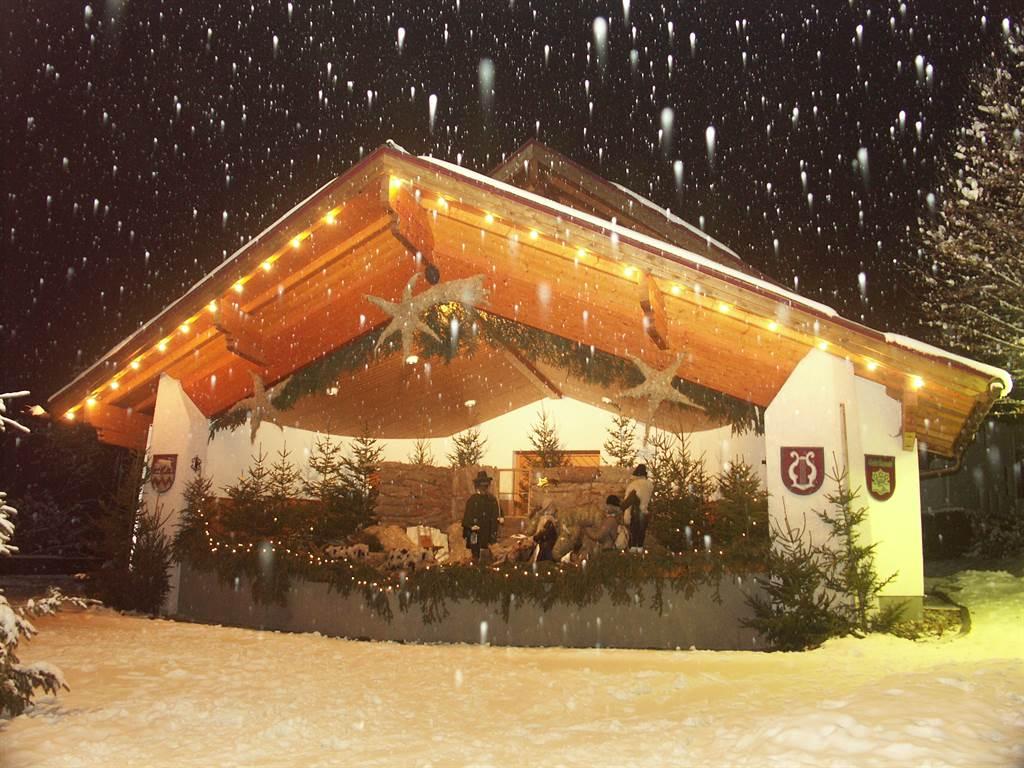 A cozy wooden house decorated for Christmas in the snow. Gently falling snow and lights create a festive atmosphere.