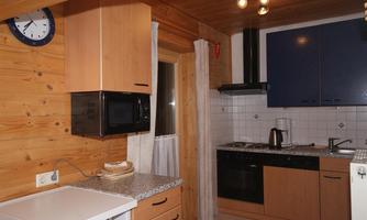 A modern kitchen with wood paneling and gray countertops. It is equipped with a refrigerator, microwave, and cooktop.
