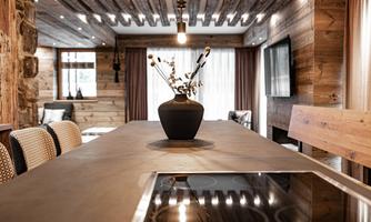 A modern kitchen with a large wooden table and a stylish vase in the center. The walls are made of warm wood, and the light creates an inviting atmosphere.
