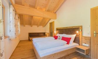 A cozy bedroom with wooden furniture and a large double bed. The bright walls and wooden floor create a warm atmosphere.