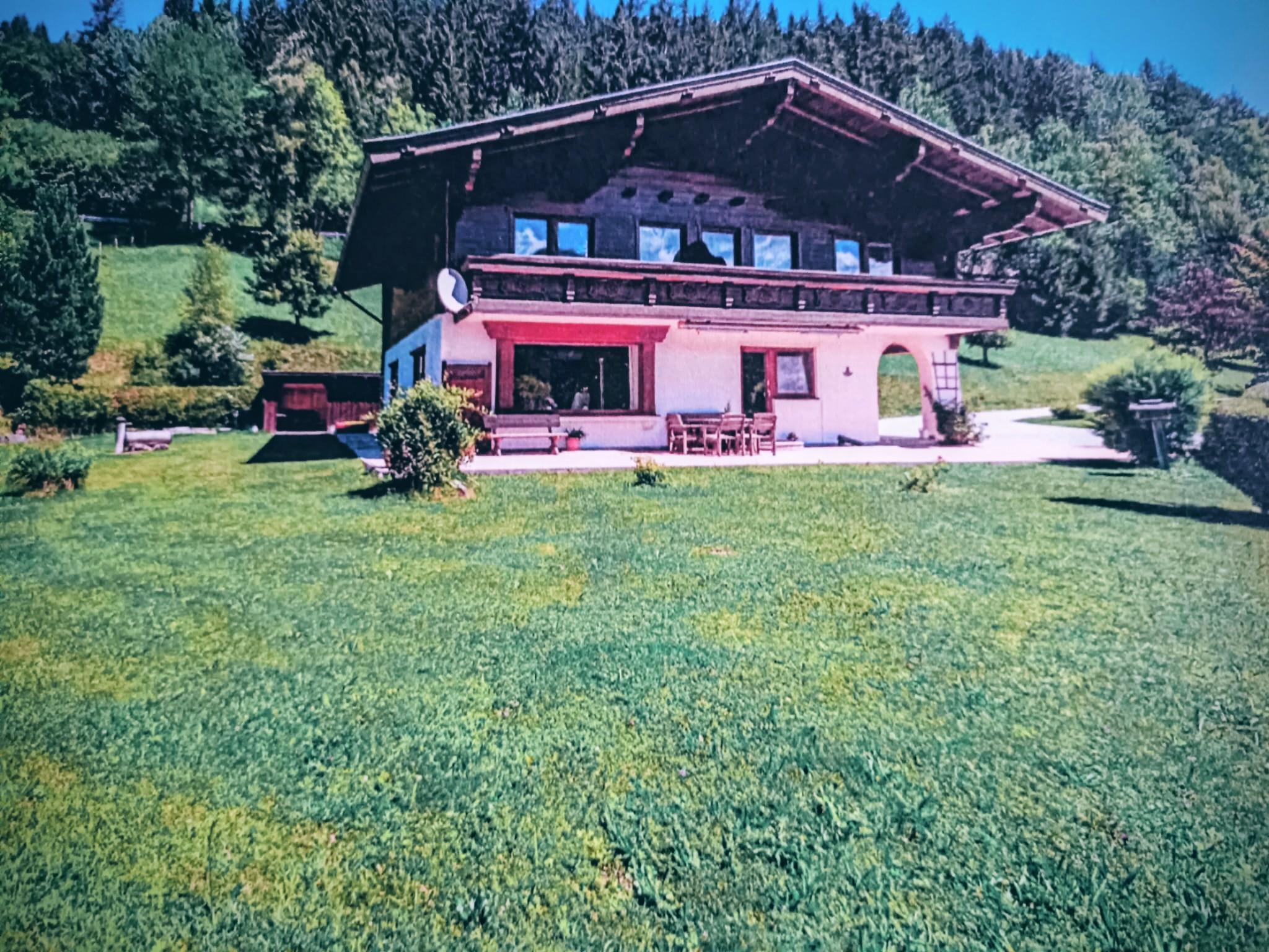 A traditional house surrounded by lush, green grass and trees. The clear blue sky creates an inviting atmosphere.