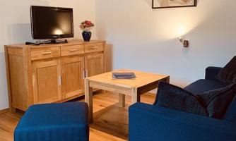 A cozy living room with a blue sofa and an ottoman. A wooden table and a television complement the decor.