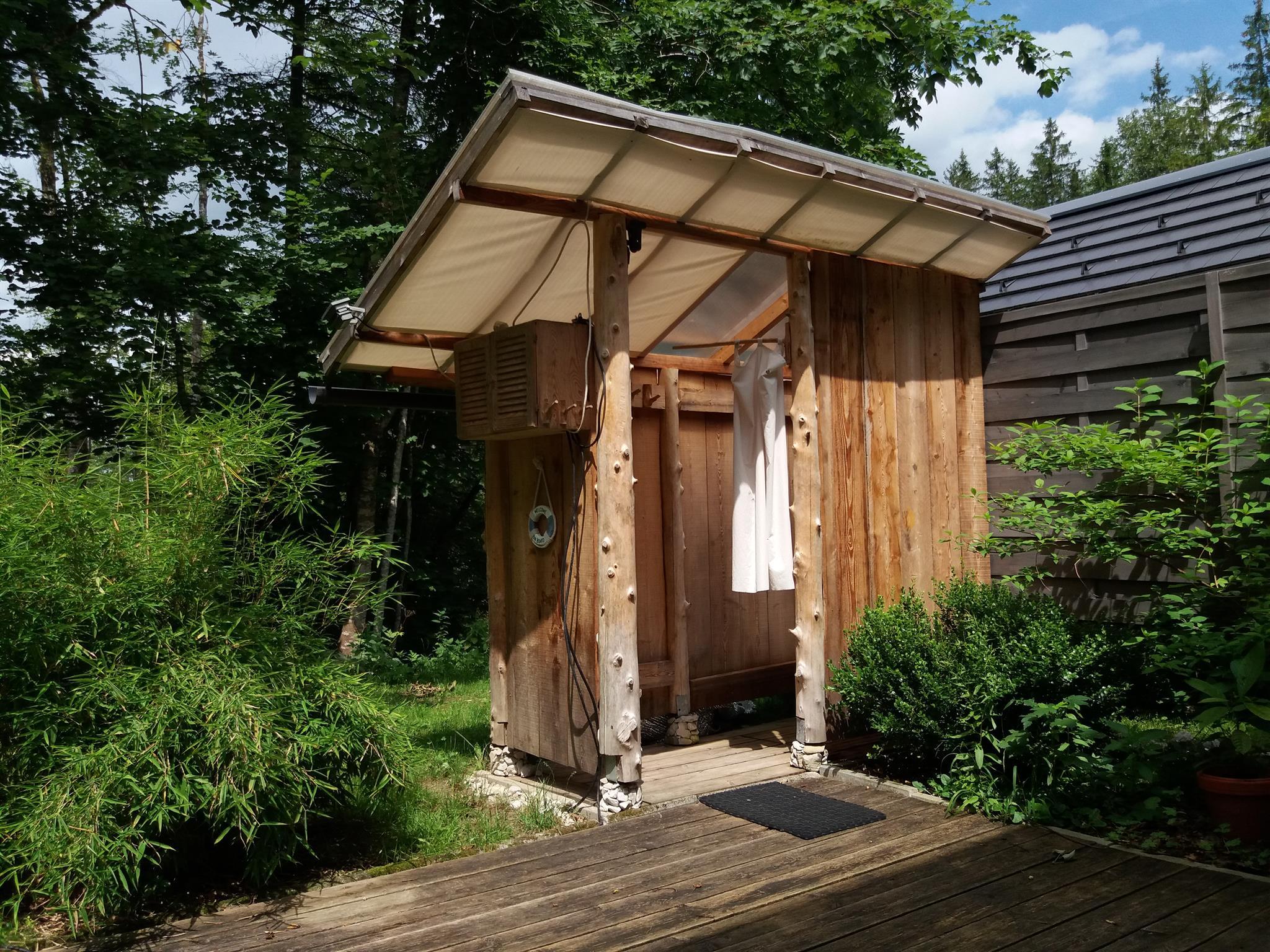 A small wooden garden shed stands amidst green plants. The entrance is open and showcases a simple, rustic style.