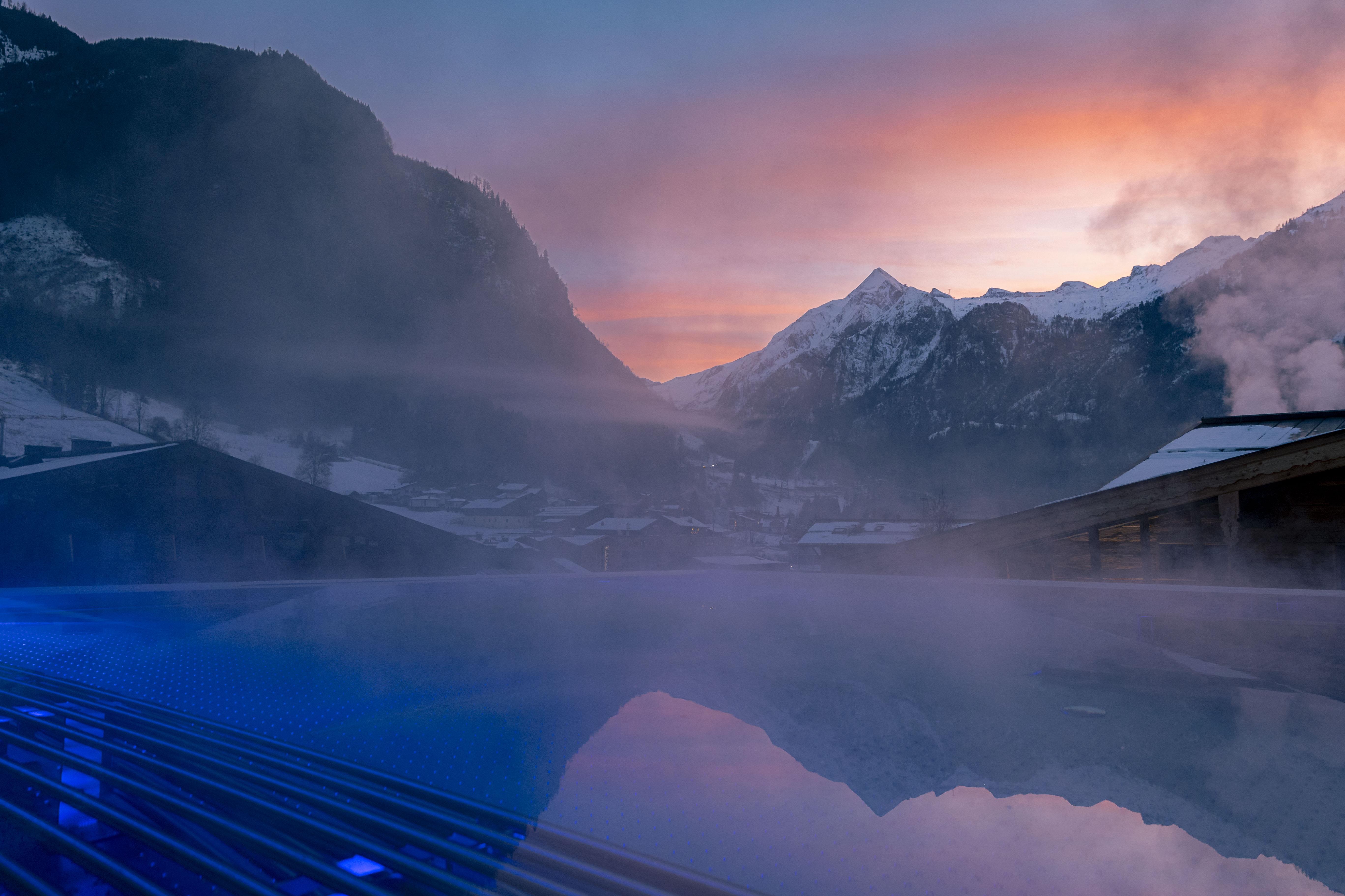 A beautiful infinity pool with steaming water in a mountainous landscape. The sunset creates a magical atmosphere with soft colors in the sky.