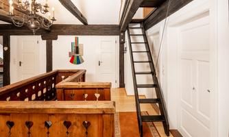 A bright entrance area with wooden paneling and a staircase. Colored decorations hang on the wall and the doors are white.