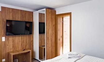 A modern room with two beds and a television on the wall. The decor is bright and warm, featuring wooden tones and a mirror.