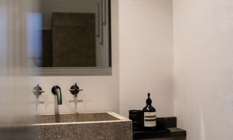 A modern bathroom with an elegant stone sink. In the background, there is a large mirror and a stylish wall design.