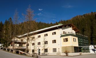 A large building in the mountains, surrounded by coniferous trees. The sky is clear and blue, ideal for a stay in nature.