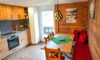 A cozy kitchen with wooden shelves and a large dining table. Red cushions and an elegant lamp create an inviting atmosphere.