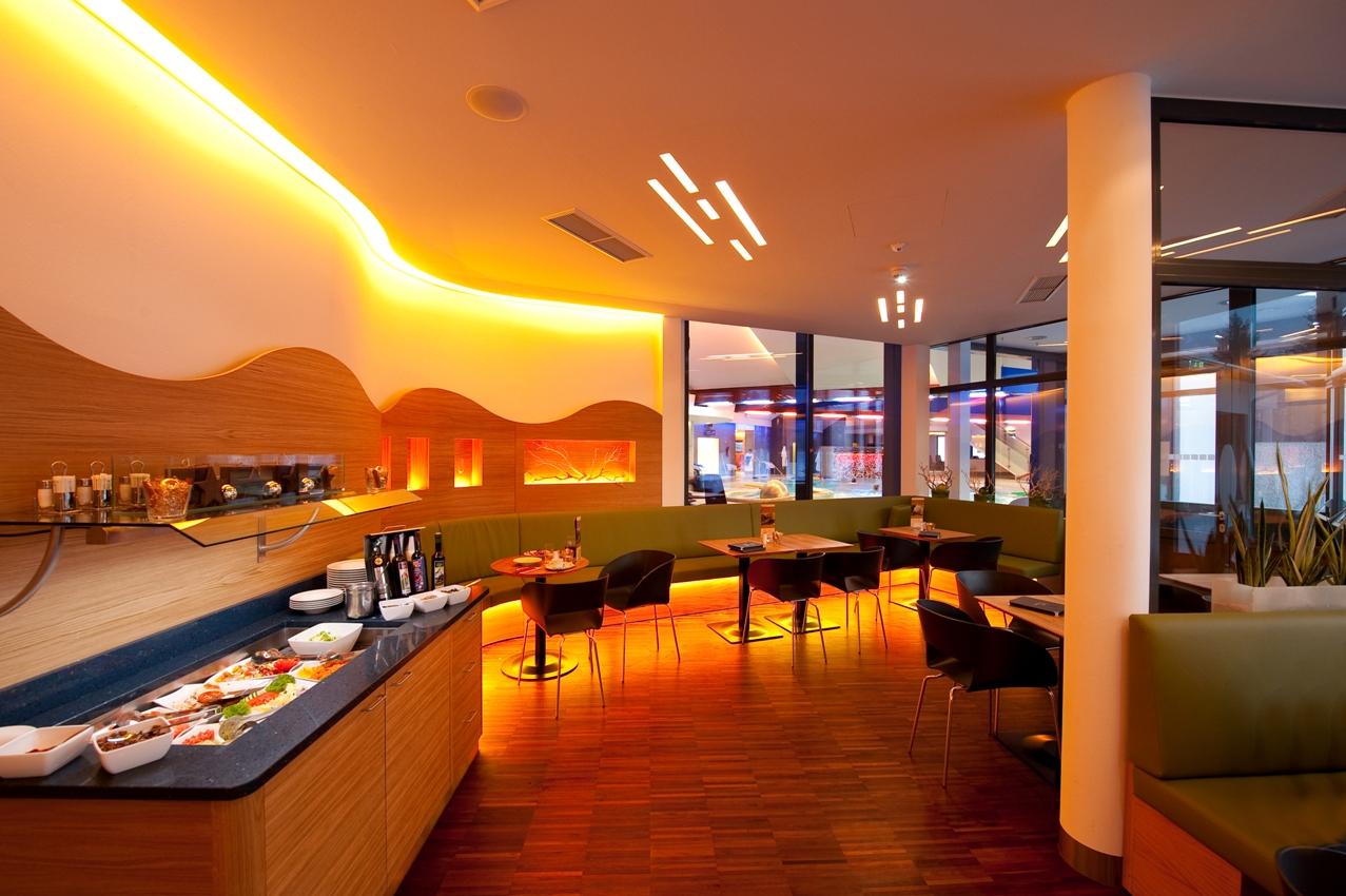 A modern restaurant with a stylish atmosphere and warm lighting. In the corner, there is a buffet with various dishes.