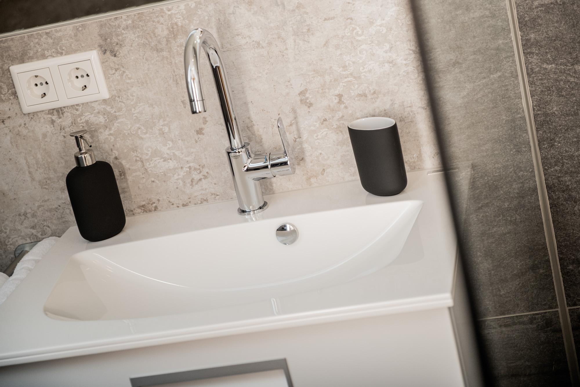 A modern sink with a stylish faucet. Next to the sink are two elegant accessories in black.