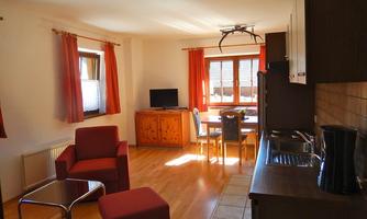 A bright, modern apartment with red curtains and cozy furniture. The open living area includes a small kitchen and a dining area with a table and chairs.