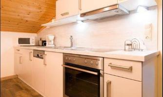 A modern kitchen with bright cabinets and a wooden ceiling. It is equipped with an oven, a microwave, and a coffee machine.