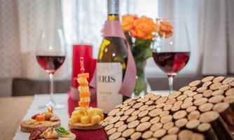 A beautifully set table with wine, two glasses of red wine, and appetizing snacks. In the background, there is a vase of roses and a decorative arrangement of wooden slices.