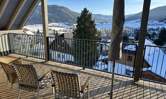 A balcony view with two chairs and a sunshade. In the background, snow-covered mountains and valleys are visible.