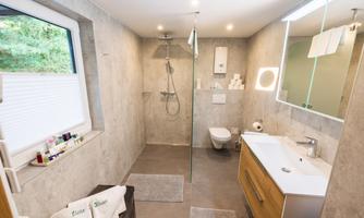 A modern bathroom with a glass shower and elegant fixtures. There is plenty of natural light and a bright, friendly atmosphere.