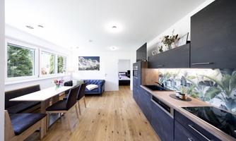 A modern kitchen with a dining table and elegant chairs. Large windows provide plenty of natural light and a view outside.