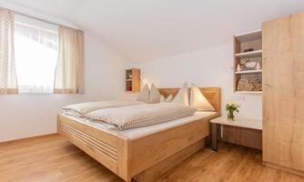 A cozy bedroom with a double bed and wooden floor. The large windows let in plenty of light and create a bright atmosphere.