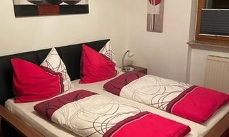 A cozy bedroom with a double bed and red pillows. Decorative pictures hang on the wall and the room has a wooden style.